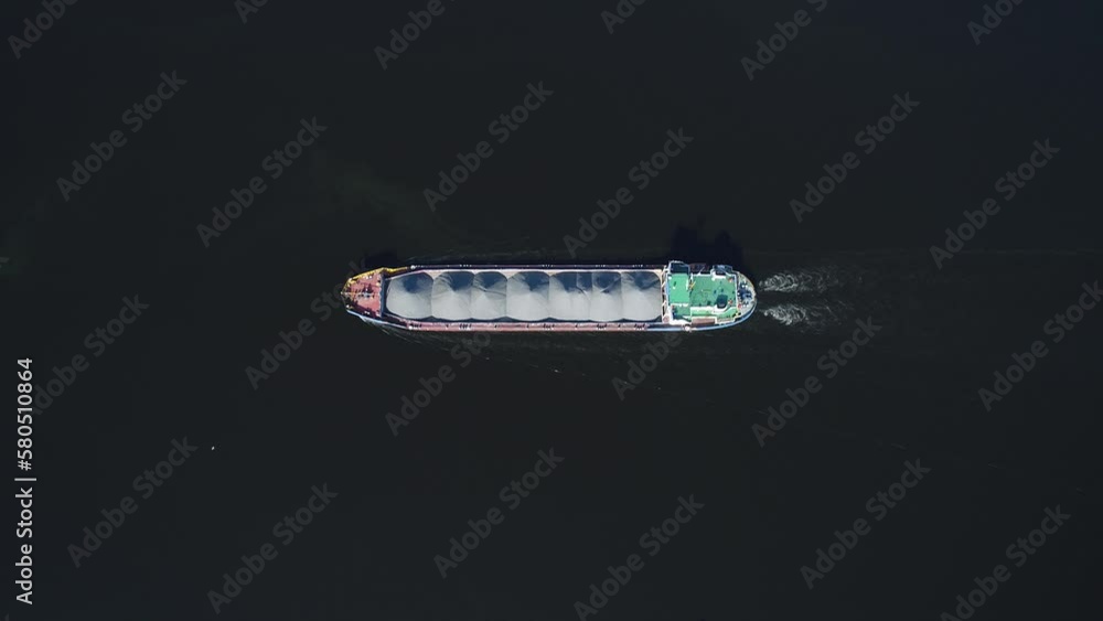 Aerial view. The barge floats on a wide river loaded with rubble. Delivery of raw materials by water. The bulk carrier transports gravel on a navigable river. Vertically view from drone. Aerial view. The barge floats on a wide river loaded with rubble. Delivery of raw materials by water. The bulk carrier transports gravel on a navigable river. Vertically view from drone.