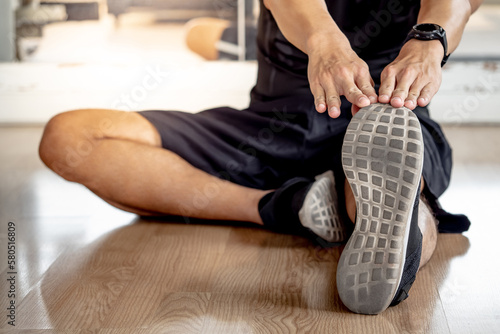 Sport man stretching legs on the floor and warming up before training in fitness gym. Physical exercise posture for muscle stretching.