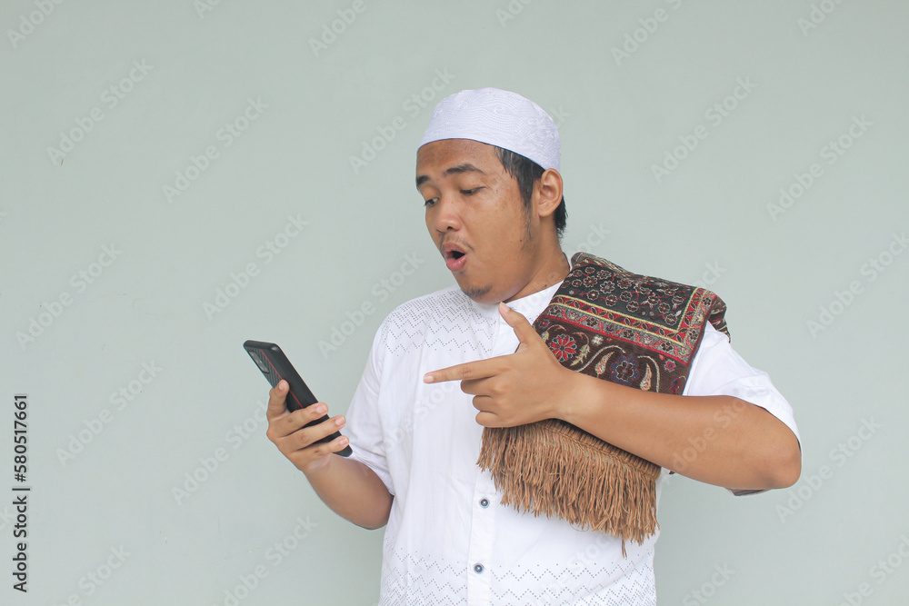 Young Asian Muslim with a shocked expression while looking at his handphone Young Asian Muslim with a shocked expression while looking at his handphone