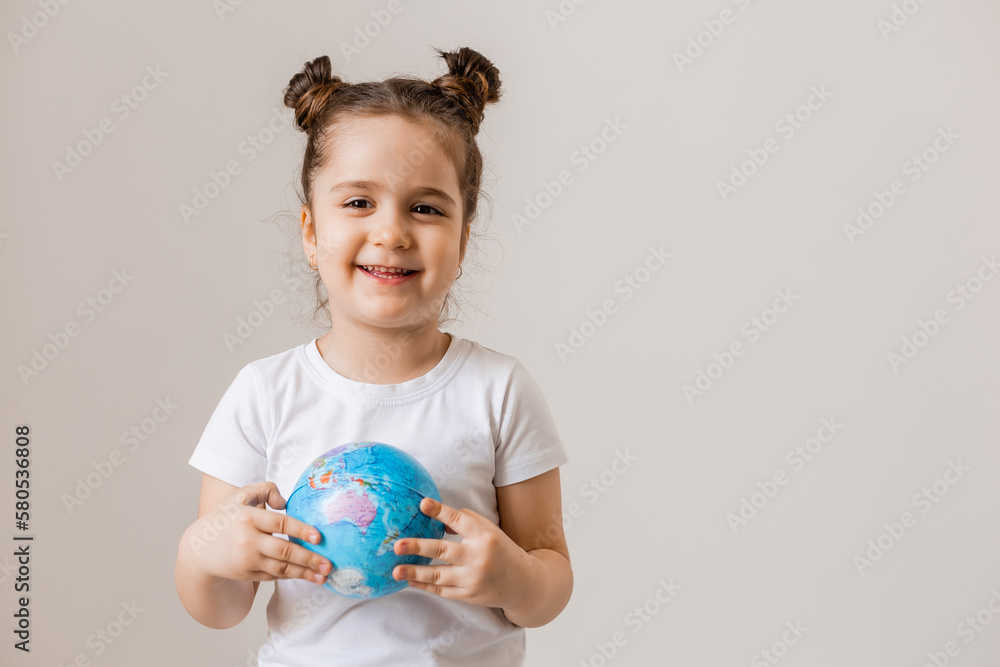 a happy little girl is holding a small globe planet in her hands in a white T-shirt on a white background. Earth Day, space for text a happy little girl is holding a small globe planet in her hands in a white T-shirt on a white background. Earth Day, space for text