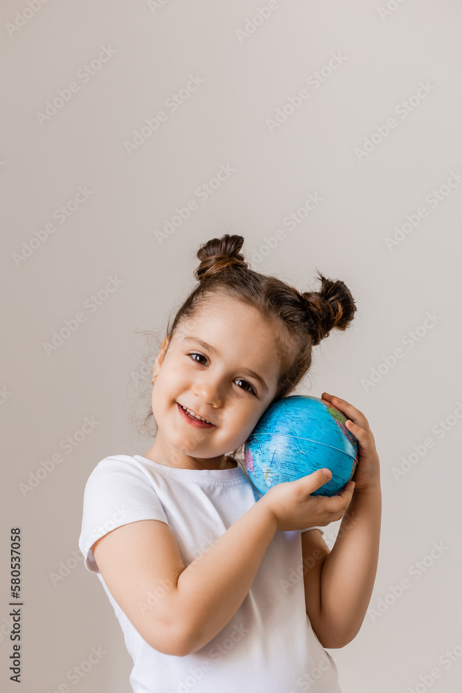 a happy little girl is holding a small globe planet in her hands in a white T-shirt on a white background. Earth Day, space for text a happy little girl is holding a small globe planet in her hands in a white T-shirt on a white background. Earth Day, space for text