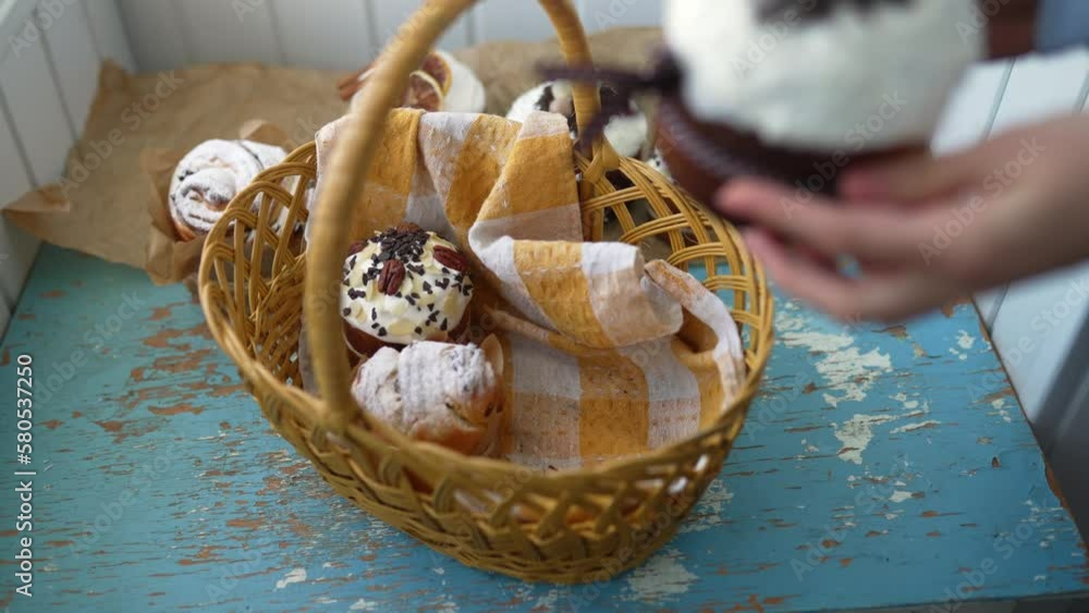 Female hands put Easter cakes creatively decorated with white icing, candied fruits, nuts and chocolate into authentic plaited basket. Stylish traditional Easter buns on linen tablecloth. Female hands put Easter cakes creatively decorated with white icing, candied fruits, nuts and chocolate into authentic plaited basket. Stylish traditional Easter buns on linen tablecloth.