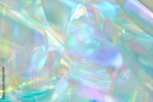 Close-up of ethereal pastel neon mint, turquoise, blue, purple, yellow holographic metallic foil background. Abstract modern curved blurred surreal futuristic disco, techno dreamlike backdrop.