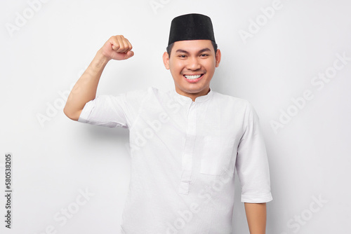 Handsome young Asian Muslim man showing arm muscle, confident and proud of power isolated on white background. People religious Islamic lifestyle concept