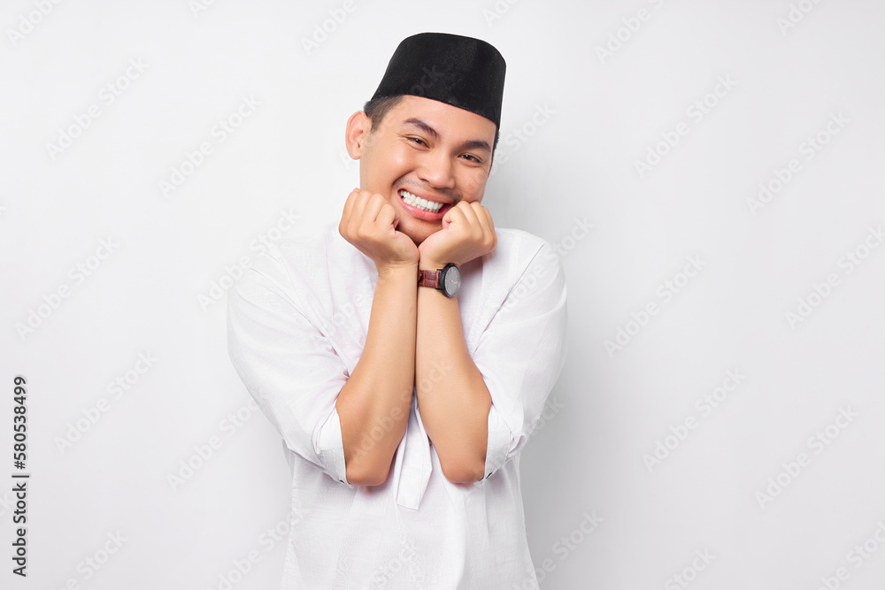 Smiling young Asian Muslim man pressing hands together under his chin isolated on white background. People religious Islamic lifestyle concept Smiling young Asian Muslim man pressing hands together under his chin isolated on white background. People religious Islamic lifestyle concept