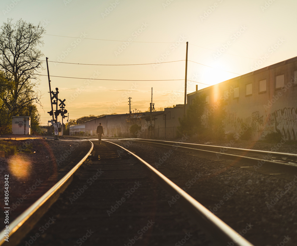Rear view of man walking on railroad track during sunset Rear view of man walking on railroad track during sunset