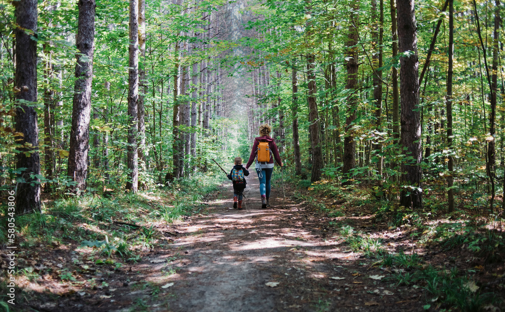Rear view of mother and son with backpack hiking in forest Rear view of mother and son with backpack hiking in forest
