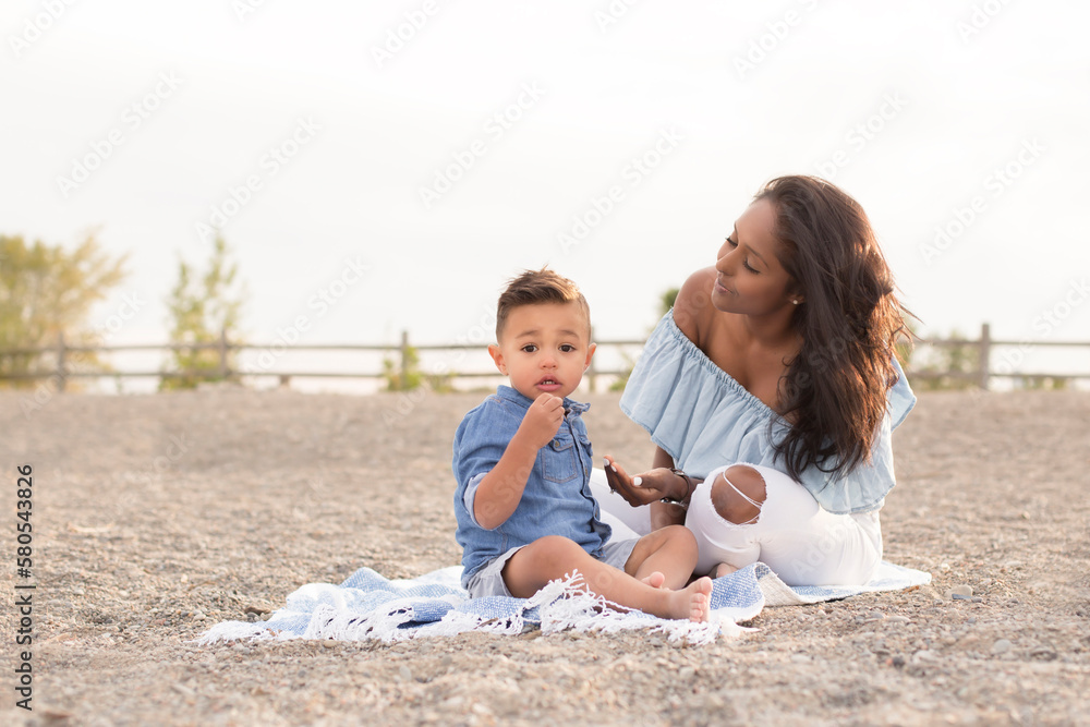 Portrait of cute son sitting with mother on picnic blanket against sky at beach