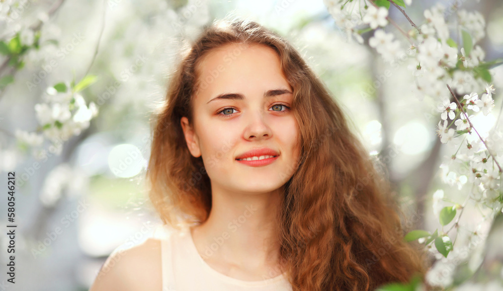 Fototapeta premium Portrait of beautiful cute young woman with long curly hair in spring blooming garden on white flowers background