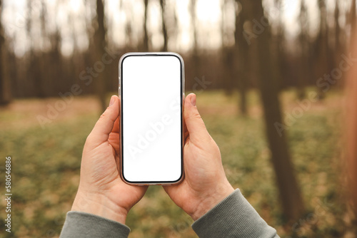 Hand holding phone with blank screen taking photo or selfie in the forest. There is no signal. The concept may relate to digital detox or business message