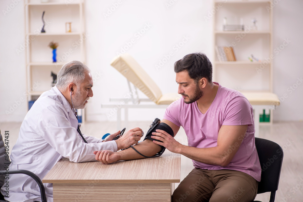 Obraz premium Old male doctor measuring young patient's blood pressure