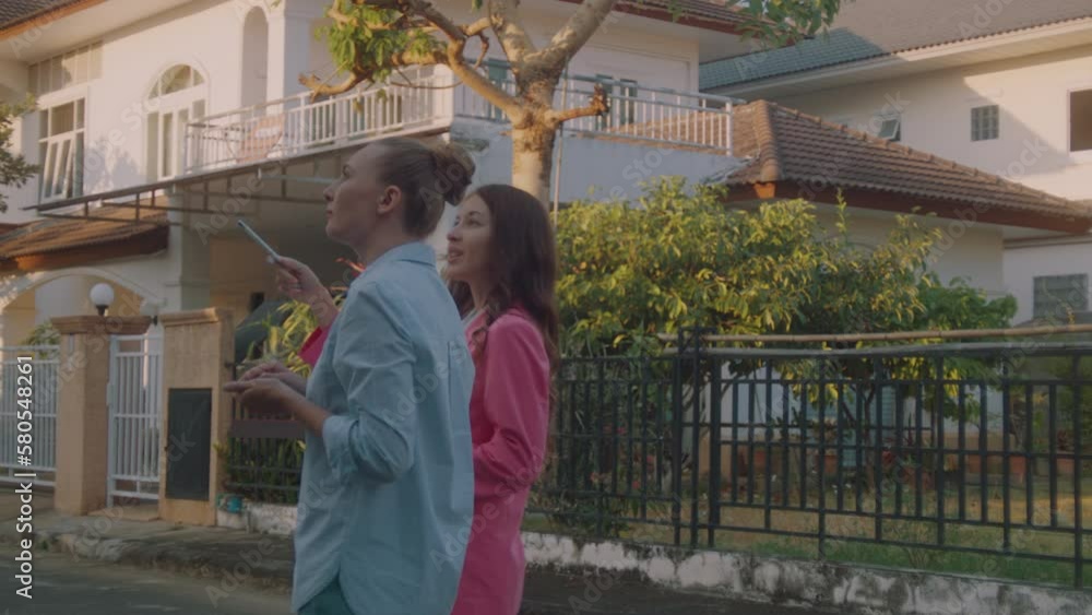 A young female real estate agent in a pink business suit with documents in hand shows houses to a potential client A young female real estate agent in a pink business suit with documents in hand shows houses to a potential client