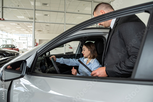 Seller with clipboard and buyer talking about purchase new car in the showroom