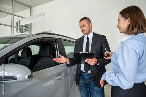 young woman standing near new modern car at the dealership and choosing the best auto with salesman