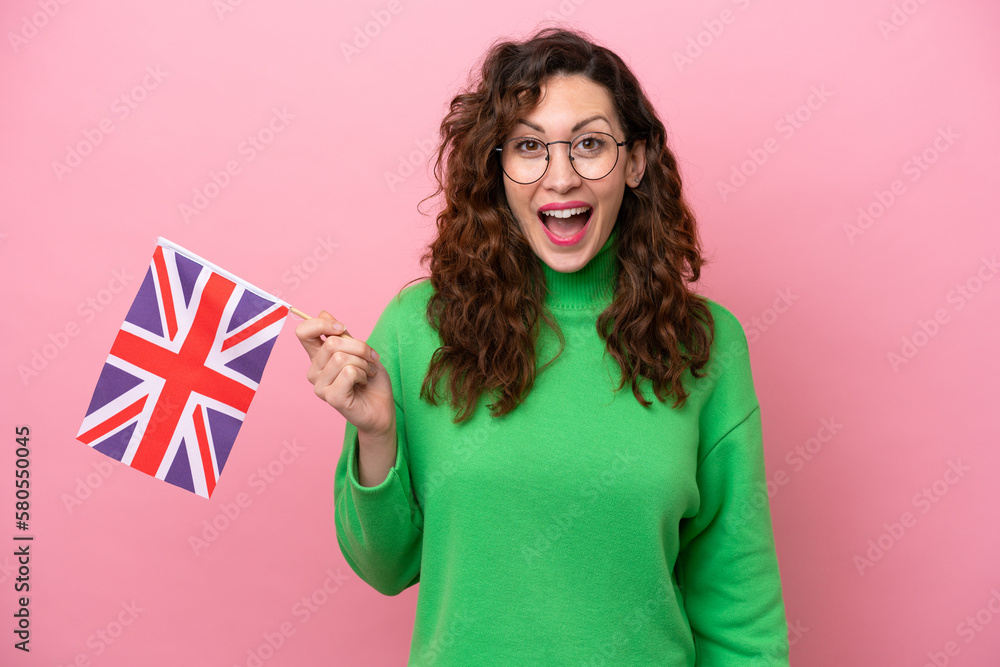 Young caucasian woman holding English flag isolated on pink background with surprise and shocked facial expression - obrazy, fototapety, plakaty 