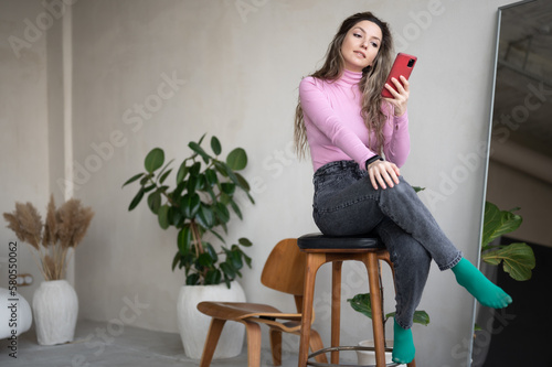 Nice attractive focused girl sitting on a wooden stool holding in hands digital device gadget spending free time.