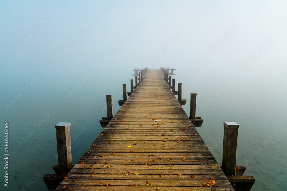 Jetty in the fog. Mystical foggy landscape at the lake. Morning fog in autumn.	