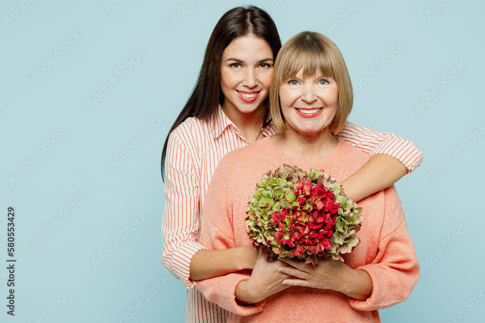Fun happy elder parent mom with young adult daughter two women together wear casual clothes hold in hand bouquet of flowers look camera hug isolated on plain blue cyan background. Family day concept. Fun happy elder parent mom with young adult daughter two women together wear casual clothes hold in hand bouquet of flowers look camera hug isolated on plain blue cyan background. Family day concept.