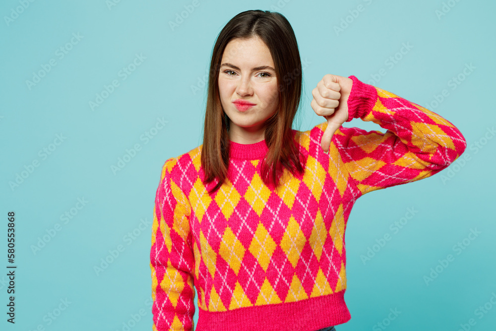 Young dissatisfied sad displeased caucasian woman wear bright casual clothes showing thumb down dislike gesture isolated on plain pastel light blue cyan background studio portrait. Lifestyle concept. Young dissatisfied sad displeased caucasian woman wear bright casual clothes showing thumb down dislike gesture isolated on plain pastel light blue cyan background studio portrait. Lifestyle concept.