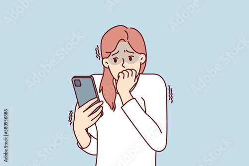 Frightened woman with phone biting nails in fear after reading bad news about approaching financial crisis. Girl with phone is afraid of threatening messages or will be on social networks 