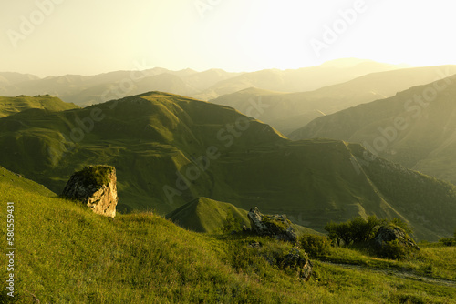 Photography Majestic summer mountain landscape - bright green mountains ridges, slopes in golden light of early morning, soft mist, lush green meadow, boulder on ledge, panorama view