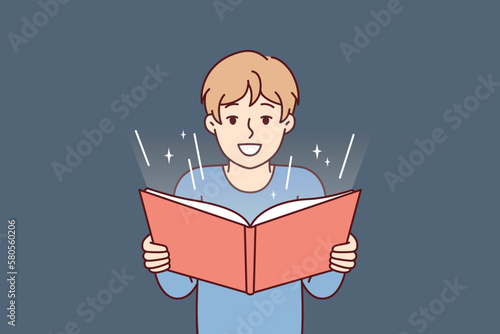 Boy before adolescence with open book in hands reads fairy tale or comics with interest. Student fulfills instructions teacher and is engaged in extracurricular activities studying material from book 