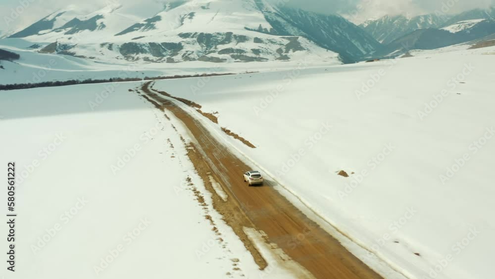 Drone tracking of a white car driving on a dirt road next to a snow-covered roadside in the mountains Drone tracking of a white car driving on a dirt road next to a snow-covered roadside in the mountains