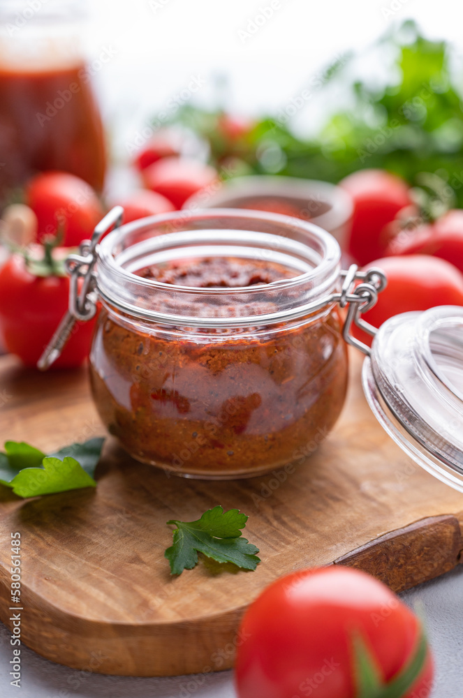 Homemade tomato sauce for pizza or pasta in a jar on a light background with fresh vegetables and herbs close up. Homemade tomato sauce for pizza or pasta in a jar on a light background with fresh vegetables and herbs close up.