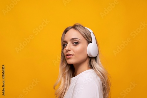 caucasian blonde woman posing in white headphones on orange background with empty space