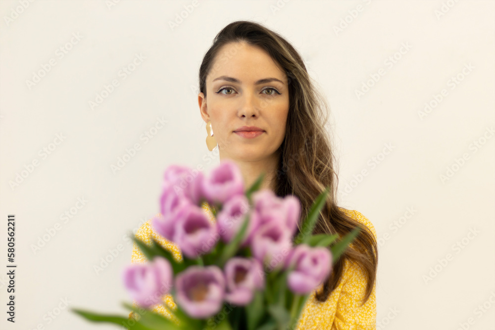 Portrait of a beautiful fashionista in yellow with a bouquet of pink tulips on a beige background. Selective focus Portrait of a beautiful fashionista in yellow with a bouquet of pink tulips on a beige background. Selective focus