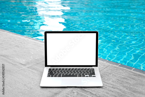 Laptop with blank screen for creative design on floor near swimming pool edge background. Computer notebook with monitor clipping path for present landing page design. Laptop computer mock up template