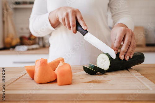 Woman with kitchen knife cutting cucumber at home photo