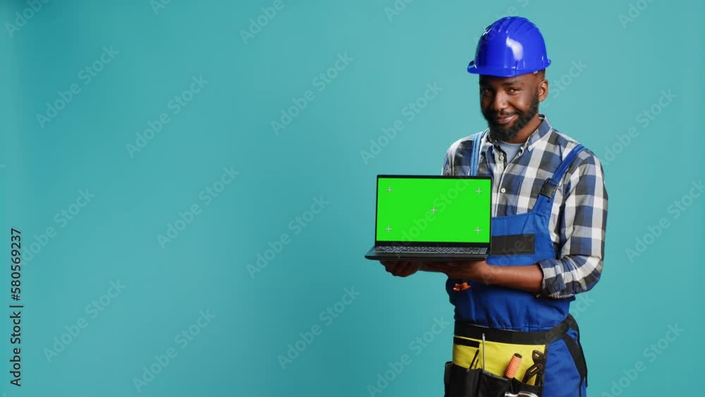 Smiling craftsman showing laptop with green screen on camera, advertising modern isolated display on pc. Young builder contractor holding computer with blank chroma key copyspace screen. Smiling craftsman showing laptop with green screen on camera, advertising modern isolated display on pc. Young builder contractor holding computer with blank chroma key copyspace screen.