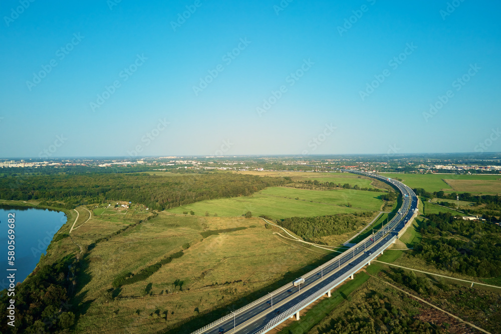 Cars driving on highway near green fields, top view. Aerial drone view of asphalt road with car traffic in countryside Cars driving on highway near green fields, top view. Aerial drone view of asphalt road with car traffic in countryside
