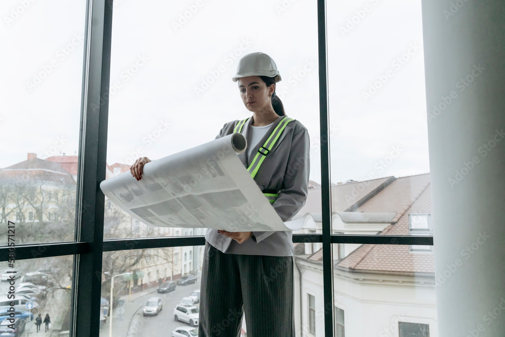 Architect reviewing blueprint standing in front of window at office Architect reviewing blueprint standing in front of window at office