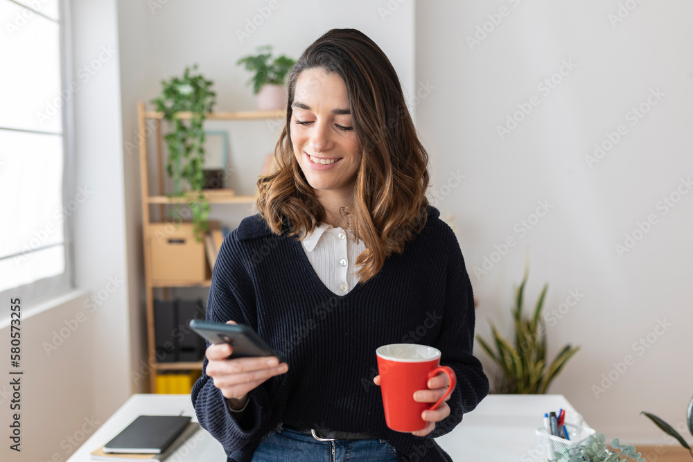 Smiling businesswoman with coffee cup using smart phone in office Smiling businesswoman with coffee cup using smart phone in office