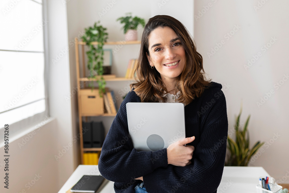Smiling businesswoman standing with laptop in office Smiling businesswoman standing with laptop in office