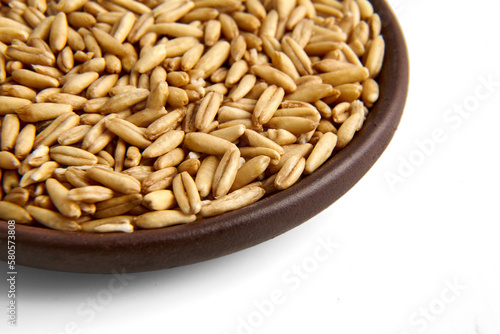 Whole grain oat groats in a clay ceramic bowl close-up isolated on a white background