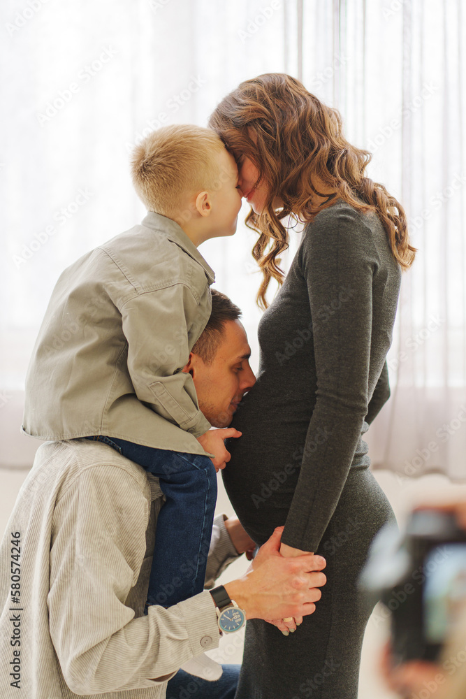 Obraz premium a loving and gentle family. pregnant mom, son sits on dad's shoulders.