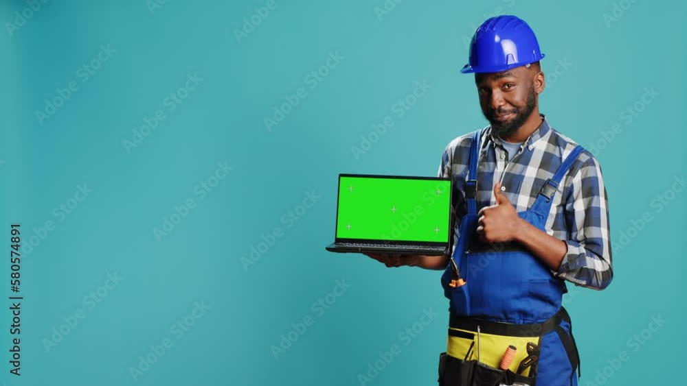 Happy mechanic pointing at laptop with greenscreen on camera, advertising isolated template display on pc. Young construction worker showing computer with chroma key mockup copyspace. Happy mechanic pointing at laptop with greenscreen on camera, advertising isolated template display on pc. Young construction worker showing computer with chroma key mockup copyspace.