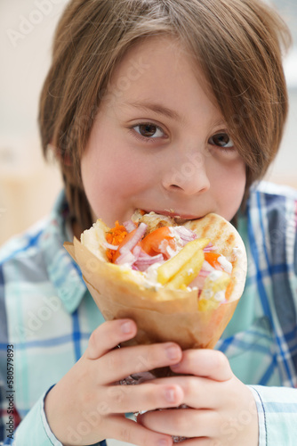Potrait of hungry little boy biting gyros. Cute elementary age kid eating Greek fast food in a restaurant.