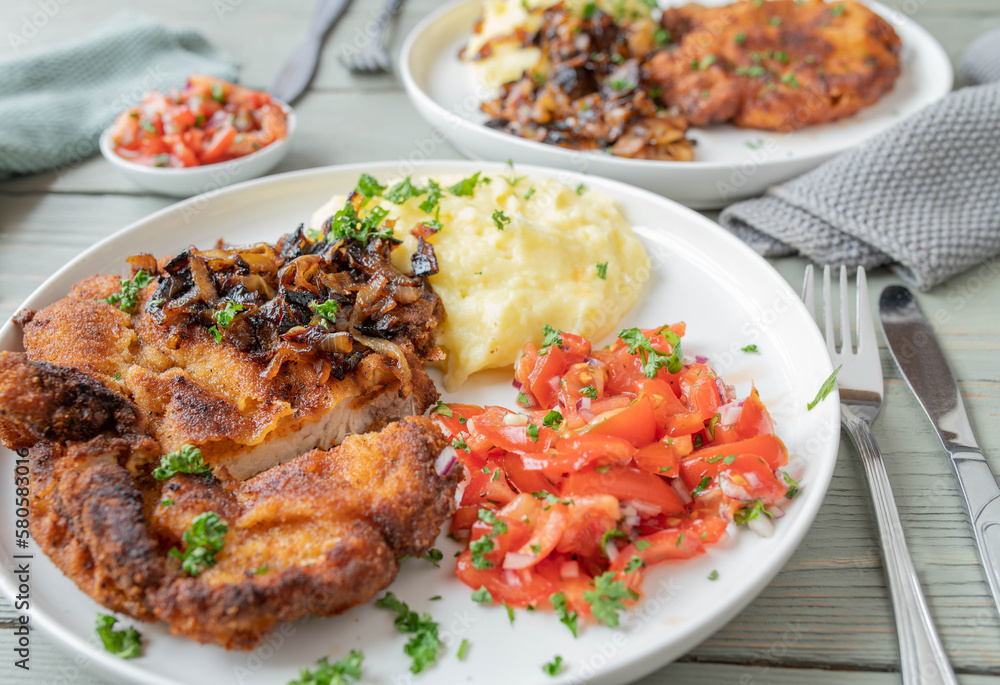 Breaded cutlet with roasted onion, mashed potatoes and tomato salad on a plate. 