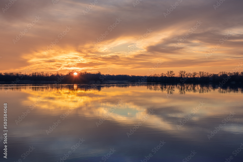Beautiful sunset with reflection of clouds on the surface of the smooth water of a wide river