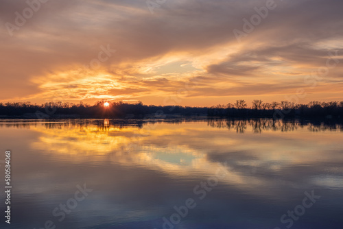 Beautiful sunset with reflection of clouds on the surface of the smooth water of a wide river