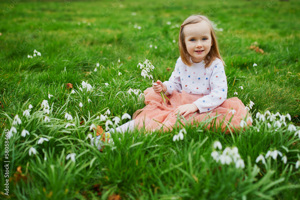 Preschooler girl in pink tutu skirt sitting in the grass with many snowdrop flowers in park or forest on a spring day Preschooler girl in pink tutu skirt sitting in the grass with many snowdrop flowers in park or forest on a spring day