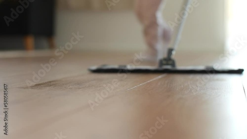 A woman using a mop to clean the apartment floor while a child walks in the background, slow motion shot