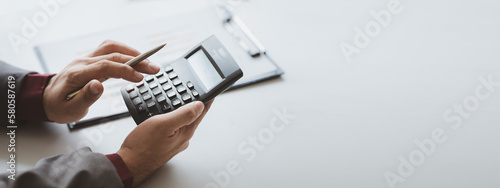 Businessman using a calculator to calculate numbers on a company's financial documents, he is analyzing historical financial data to plan how to grow the company. Financial concept.