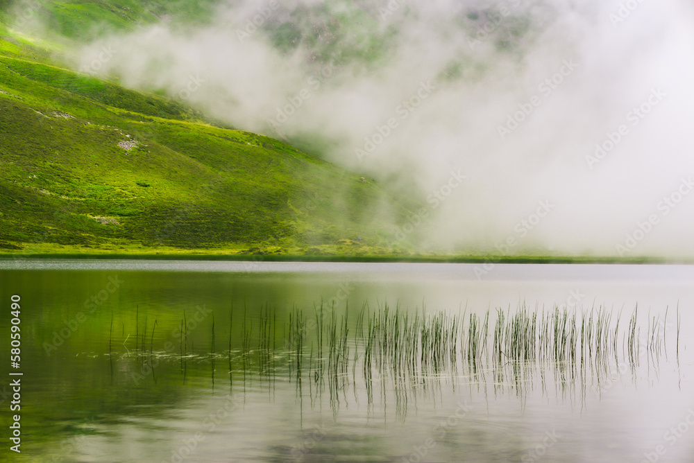 Reflection on Lake Isaby which is located on the heights of the Hautacam resort in the Pyrenees. Lake surrounded by mist. Quiet scene.