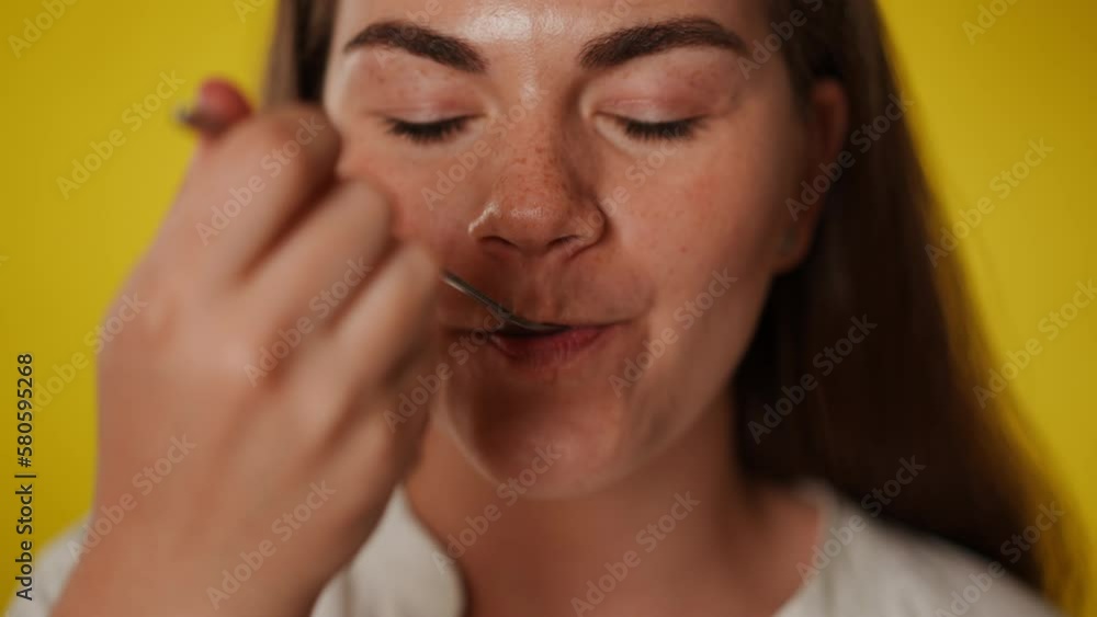 Headshot of satisfied young woman enjoying tasty smoothie in slow motion looking at camera. Front view close-up portrait of smiling beautiful lady eating posing at yellow background Headshot of satisfied young woman enjoying tasty smoothie in slow motion looking at camera. Front view close-up portrait of smiling beautiful lady eating posing at yellow background