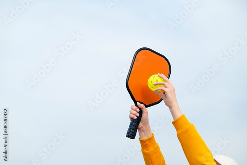 pickleball game, hands over blue sky hitting pickleball yellow ball with paddle, outdoor sport leisure activity